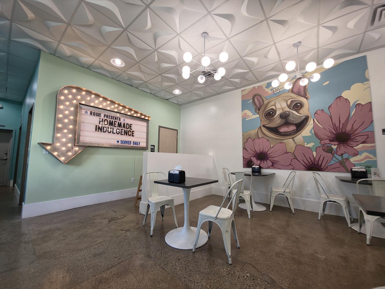 The seating room at Rosie's Ice Cream with a lit marquee sign and a mural of Rosie the French Bulldog